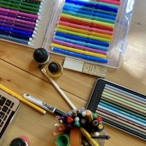 A wooden desk features Art Therapy supplies—colorful marker sets, colored pencils, ink bottles, brushes—and a blank sheet with a laptop, ideal for creative sessions or anyone searching for art therapy near me.