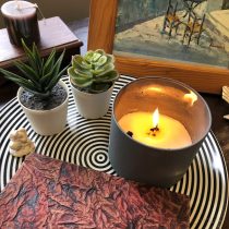 Dynamic Counseling and Coaching is displayed on a black-and-white striped tray alongside a lit candle, two potted succulents, a textured notebook, and a figurine. In the background are a brown candle, framed art, and decor.