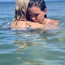 Two people embrace in calm ocean waves under a clear sky, embodying the peaceful moment captured by Intuitive Healing.