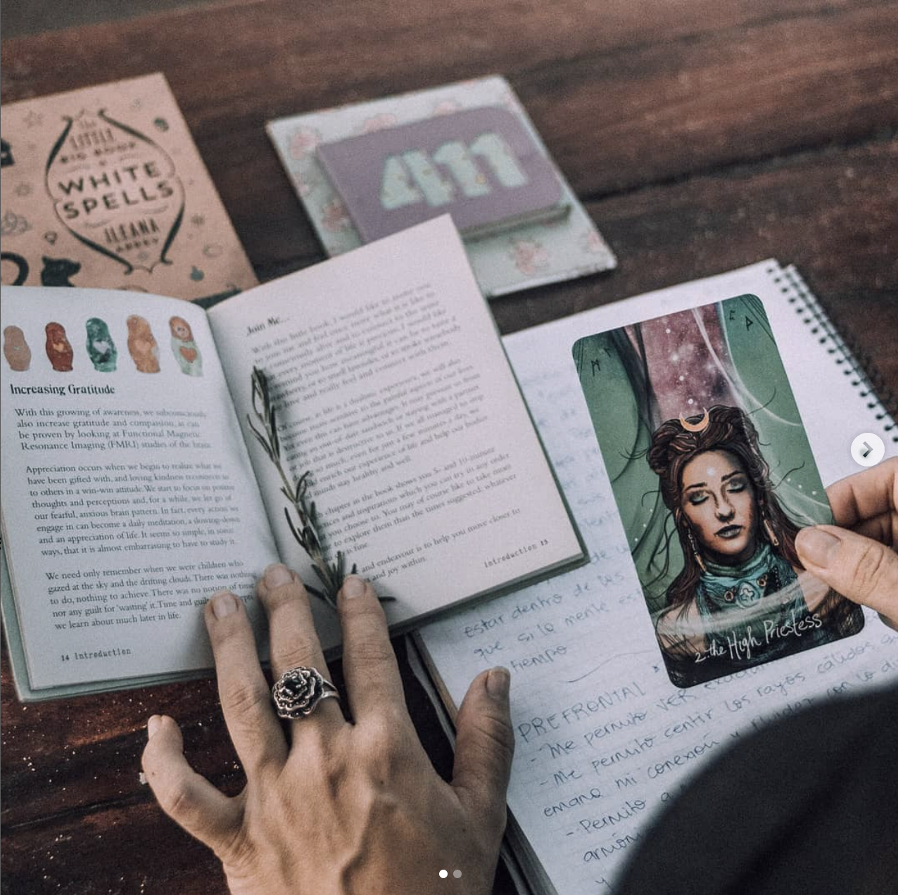 A person enjoys “Energy Healing Session & Guided Meditation” at a desk with a tarot card, handwritten notes in a spiral notebook, the book “White Spells,” and a pastel folder labeled 411—exploring gratitude and healing.