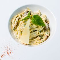 Creamy pasta topped with a slice of parmesan cheese and a fresh basil leaf in a white bowl, representing a meal from a Nutrition Health Assessment & Plan.