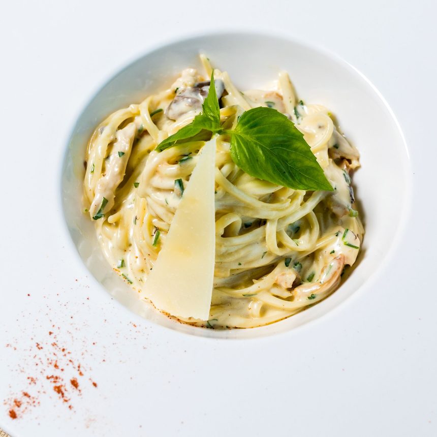 Creamy pasta topped with a slice of parmesan cheese and a fresh basil leaf in a white bowl, representing a meal from a Nutrition Health Assessment & Plan.