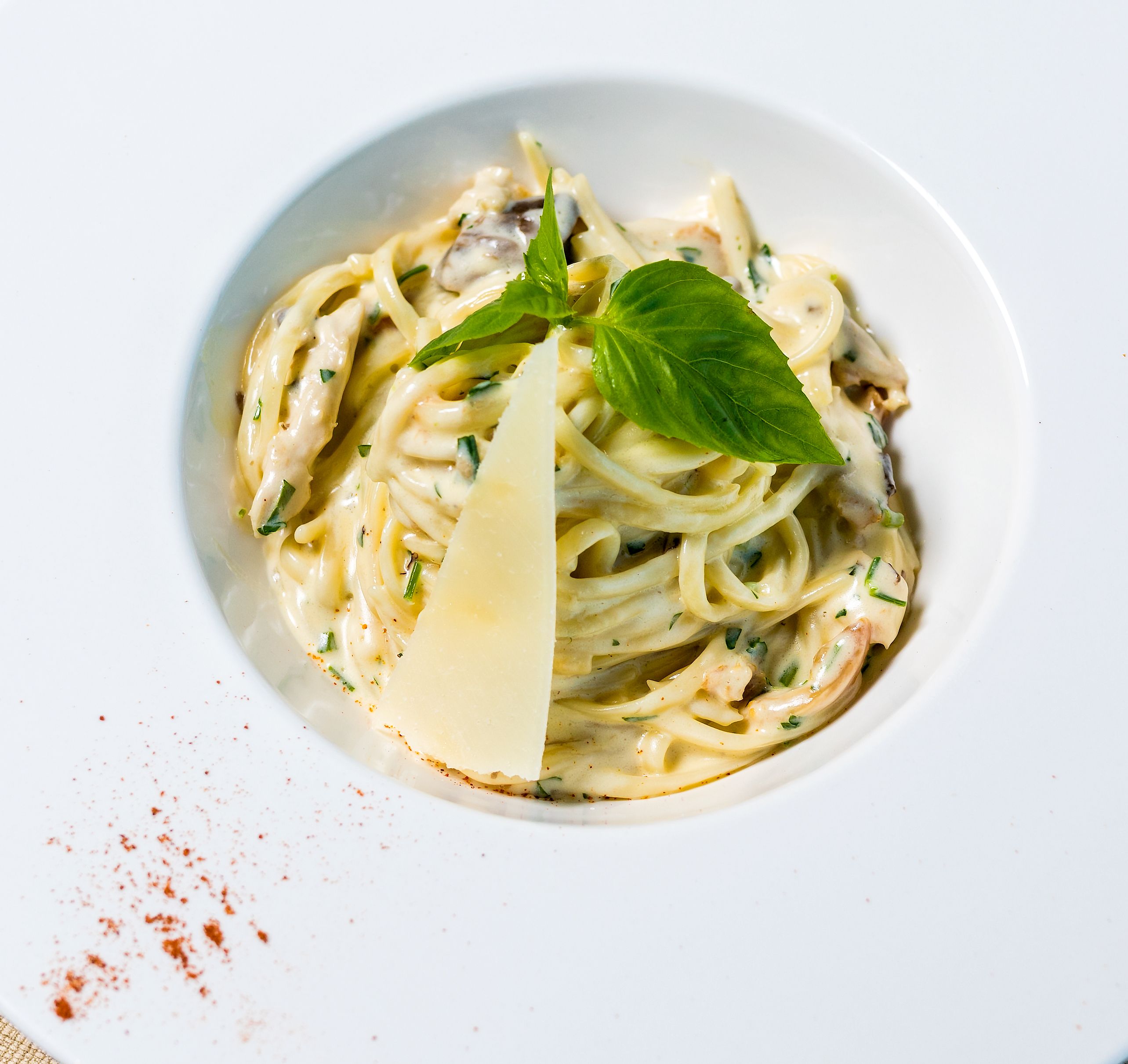 Creamy pasta topped with a slice of parmesan cheese and a fresh basil leaf in a white bowl, representing a meal from a Nutrition Health Assessment & Plan.
