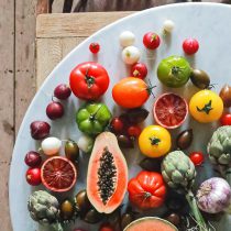 A vibrant mix of tomatoes, radishes, artichokes, onions, and papaya on a white plate—an inviting display ideal for the 3-Month Mind + Body Reset personalized nutrition coaching sessions.