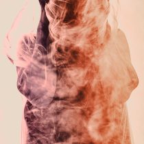 A person shrouded in sheer fabric holds their head, surrounded by vivid orange and white smoke, capturing the intense and mysterious atmosphere of navigating loss with Grief Healing.