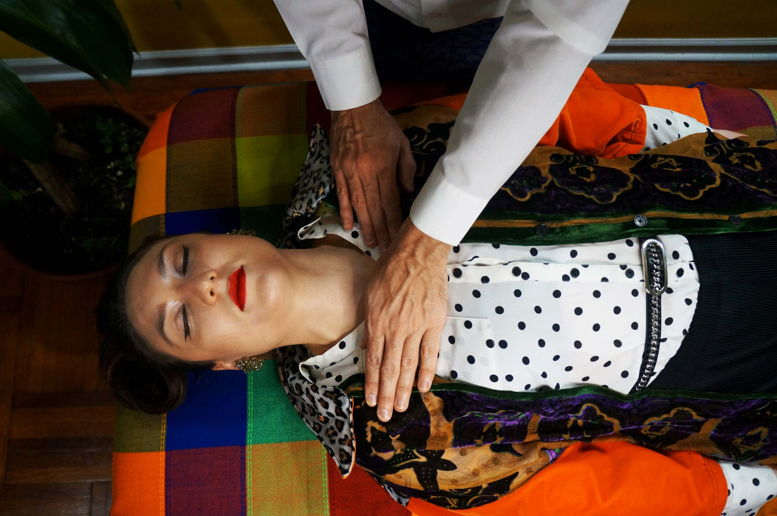 Boshko, a reiki healing practitioner, has his hand hovering over the heart of a woman who is laying down with her eyes closed.