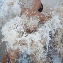 A person leans back in water while large splashes and waves cascade around them, partially obscuring their body and creating a dramatic, dynamic effect.