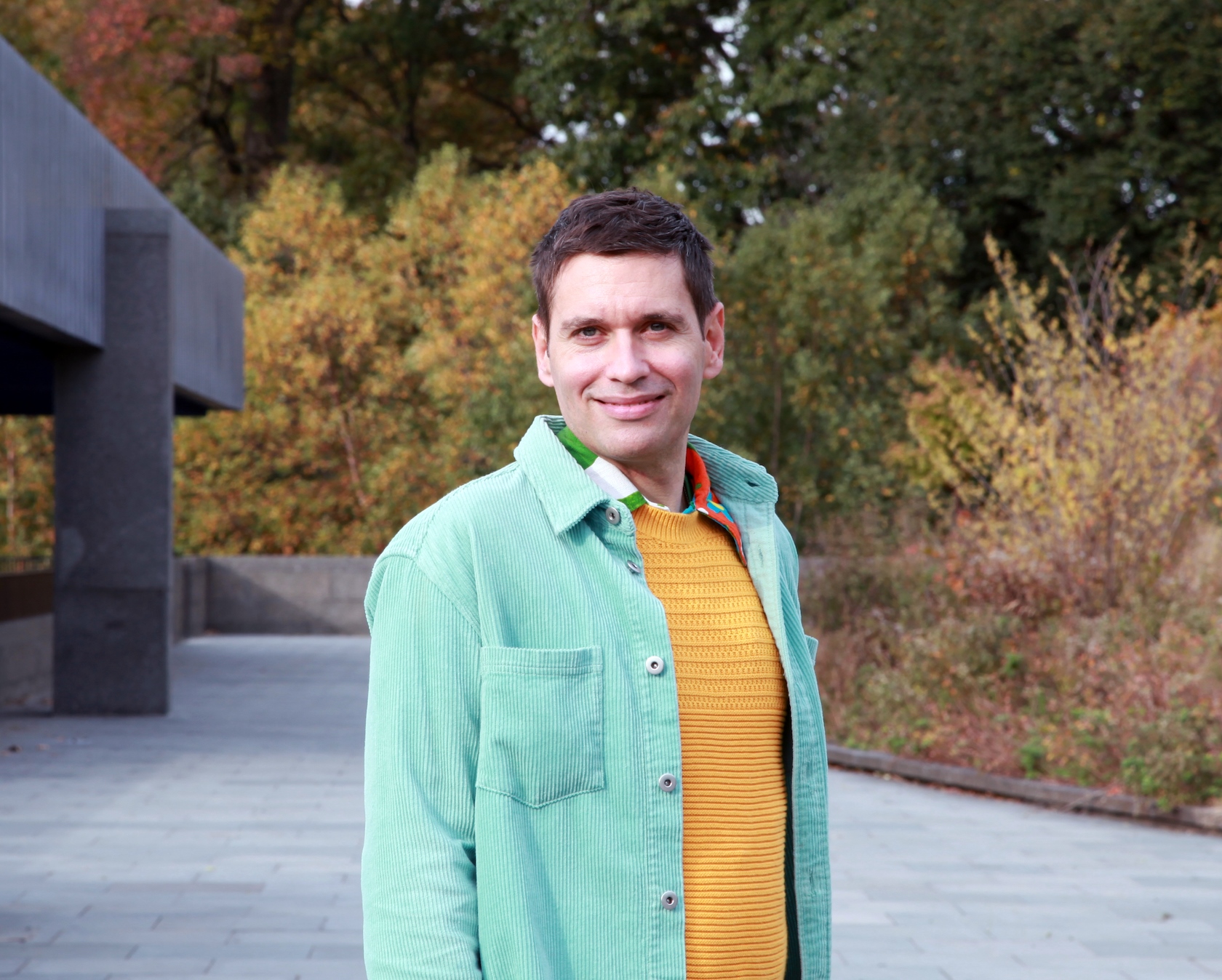 Boshko is wearing a bright yelllow knitted sweater underneath and unbuttoned turquoise corduroy longsleeve shirt. Boshko leads reiki and sound healing sessions for groups.