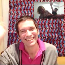 A smiling man waves at the camera during a video call. In the corner, a couple also wave and smile from a bright room filled with the calming energy of Reiki & Sound Meditation.