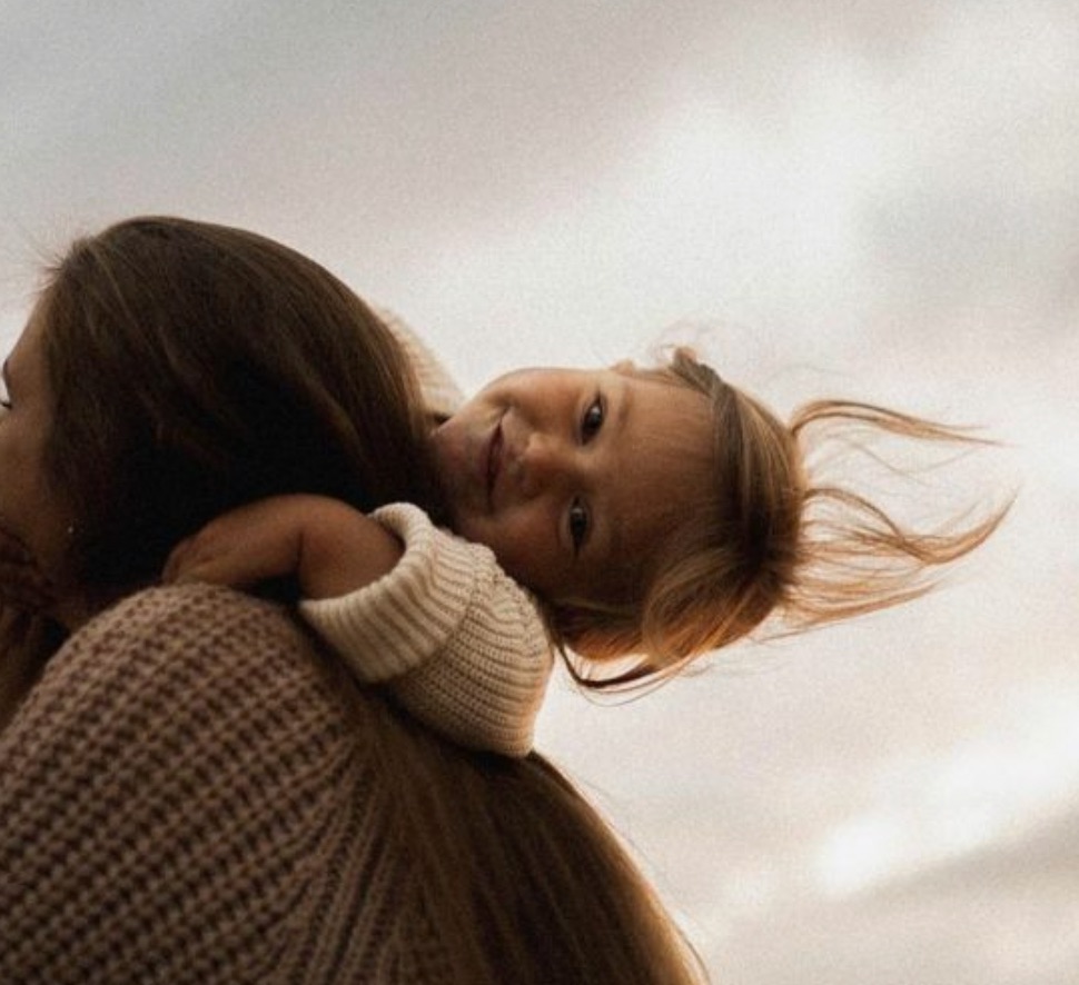 A person with long dark hair is holding a young child over their shoulder. This image represents the Parenting with Purpose online course.