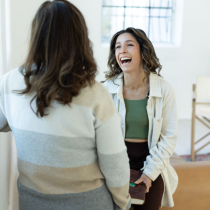 Two women enjoy a lively conversation in a bright indoor space. One, likely a coach, smiles warmly—capturing the supportive atmosphere of the 2-Month Life Purpose Coaching Program.