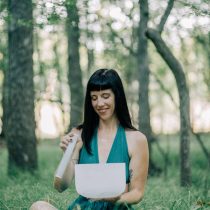 Sara is sitting in a forest wearing a green dress and holding a crystal sound bowl. This image represents her sound bowl session with intuitive guidance.