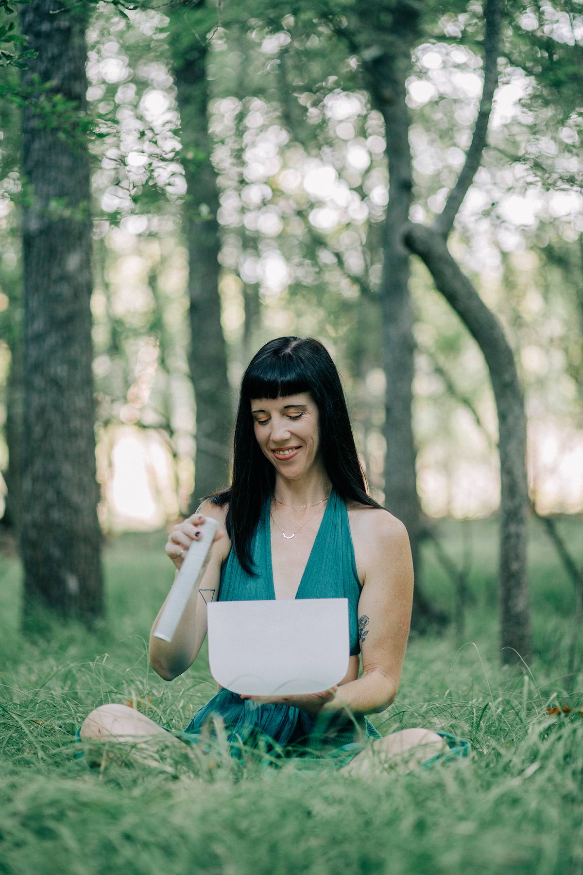 Sara is sitting in a forest wearing a green dress and holding a crystal sound bowl. This image represents her sound bowl session with intuitive guidance.