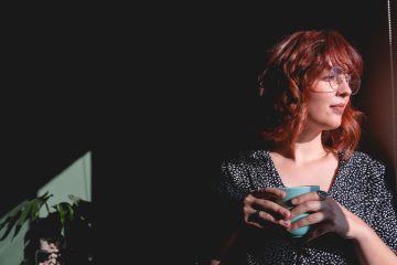 Woman holding a cup and reflecting by a sunlit window