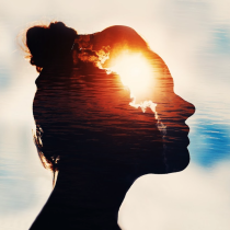 A shadow of a the profile of a woman's face is transparent towards her forhead where you see clouds from behind the face shining through. This image depicts the experience of developing your intuition.