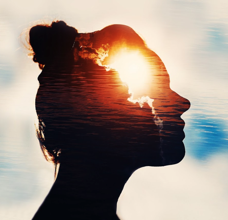 A shadow of a the profile of a woman's face is transparent towards her forhead where you see clouds from behind the face shining through. This image depicts the experience of developing your intuition.