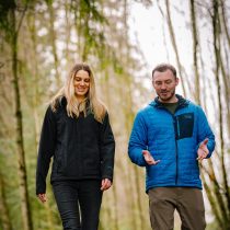 Male adventure coach walks alongside female client in the forest.