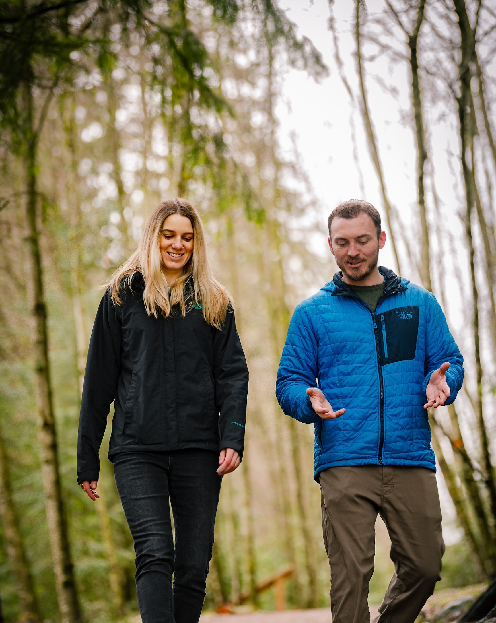 Male adventure coach walks alongside female client in the forest.