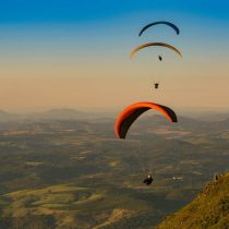 During an adventure training course, three paragliders fly over a green landscape.