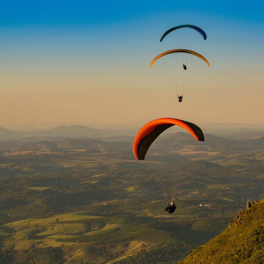 During an adventure training course, three paragliders fly over a green landscape.