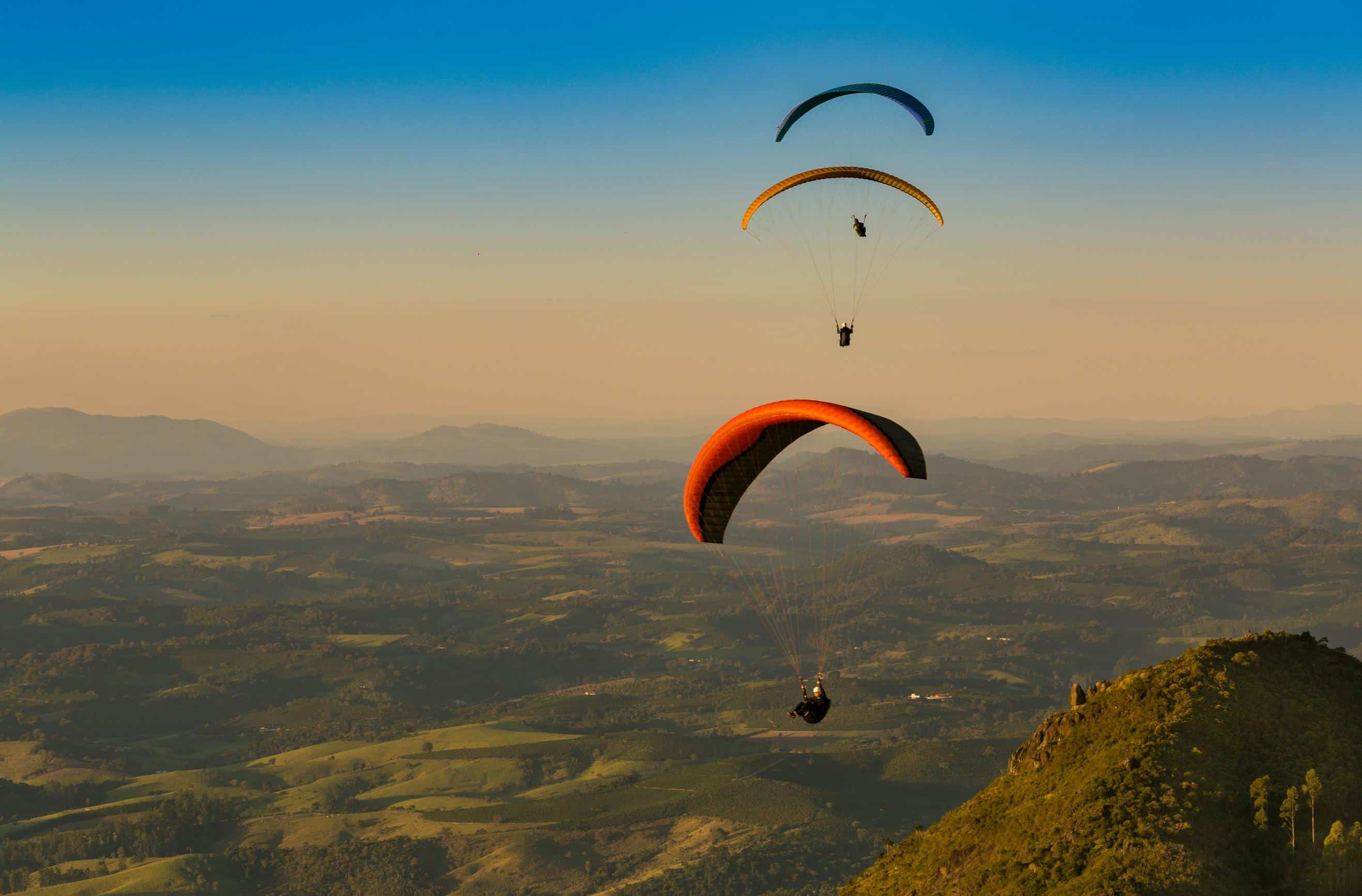 During an adventure training course, three paragliders fly over a green landscape.