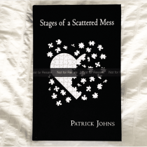 A book titled Stages of a Scattered Mess by Patrick Johns rests on a white quilt. The cover shows a heart-shaped puzzle with scattered pieces on a black background.