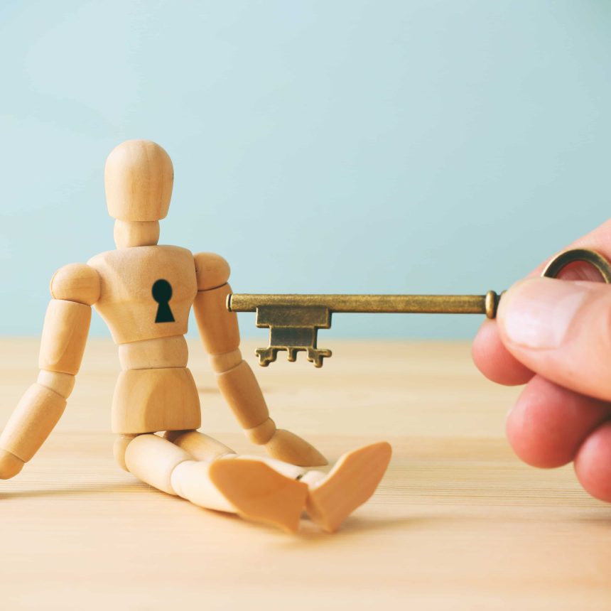 A hand is holding a key up to a keyhole in a wooden figure. This image depicts a CliftonStrengths Coaching session.