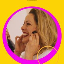A woman with blonde hair smiles brightly, holding her face with both hands against a yellow background with FALL IN LAUGH at the top and a pink border—ideal for promoting Laughter As A Tool for group stress relief activities.