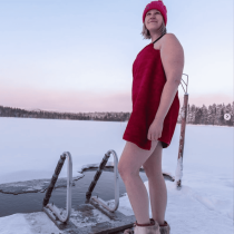 A person in red sauna attire stands barefoot on snowy ground by a frozen lake—capturing the authentic vibe of "Finnish Sauna Secrets from Lapland" amid a serene, pastel-hued winter landscape.