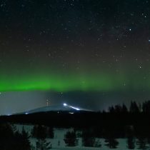 The Mystical, Magical Northern Lights glow in a starry night sky above dark hills, scattered trees, and distant lights, creating a captivating aurora borealis scene.
