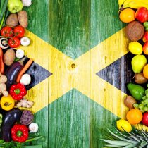 A vibrant display of fruits and vegetables lines a wooden surface painted with the Jamaican flag, highlighting Cook with Jamaicans.
