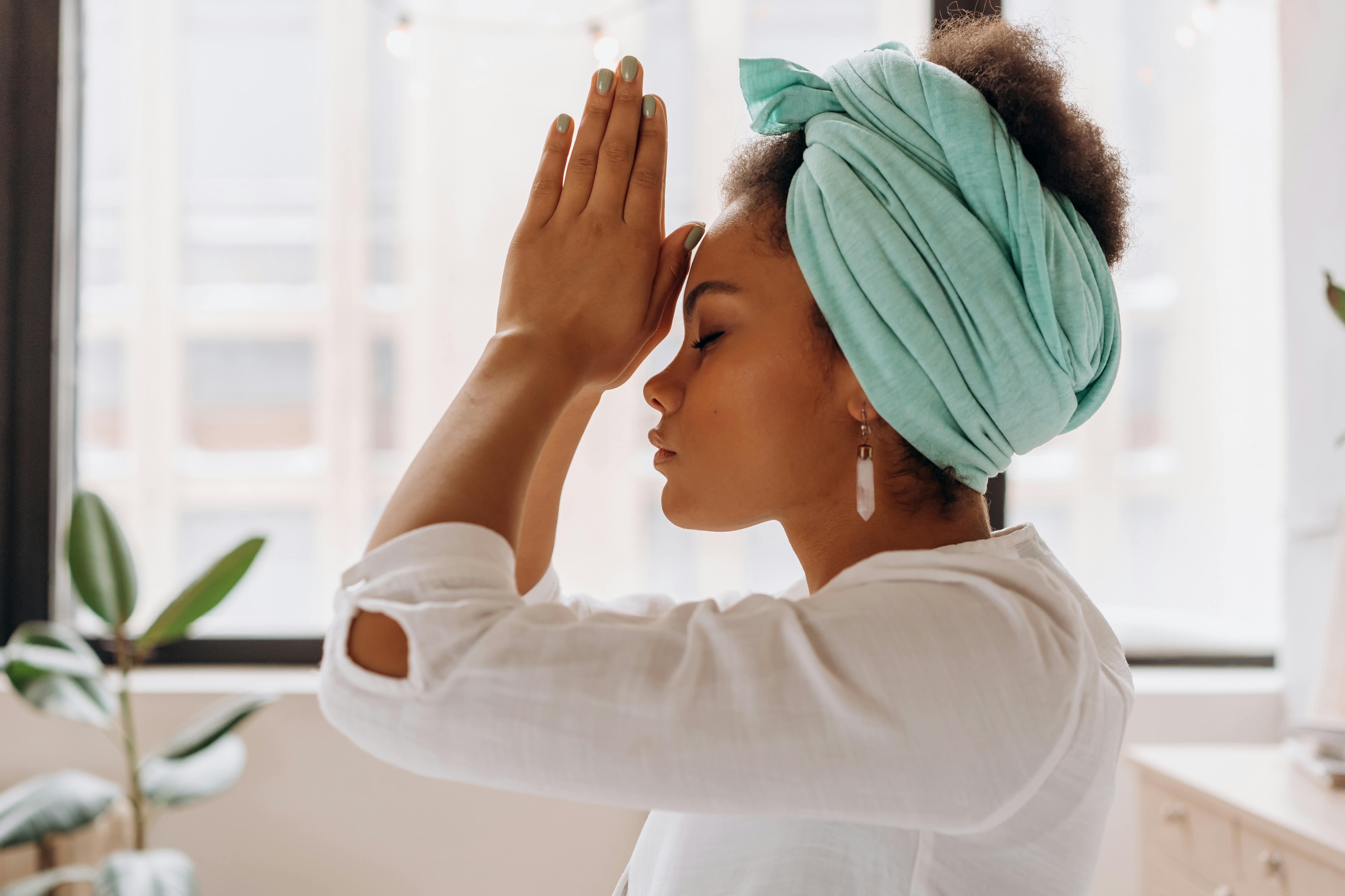 a woman has her palms touching with her thumb knuckles pressed against her forehead representing a reiki healing practice