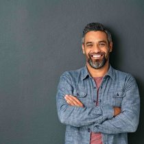 Man leaning against wall with crossed arms. Smiling at camera.