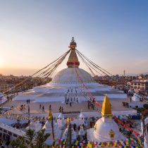 A large white stupa adorned with colorful prayer flags and a golden spire overlooks the city at sunset—an inspiring scene for anyone preparing for the Everest Base Camp Trek 2026.