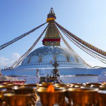 The image features the Annapurna Base Camp Trek Nepal, capturing colorful prayer flags and rows of butter lamps beneath a clear blue sky—a serene scene you may encounter on this Himalayan adventure.