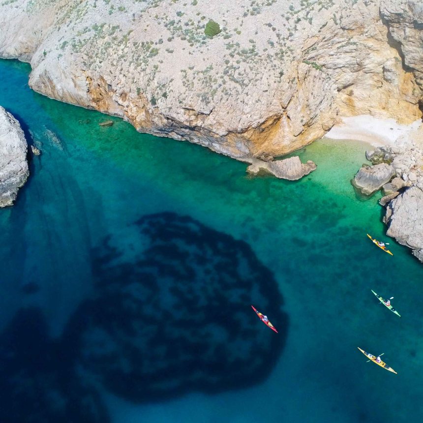 Four sea kayakers paddling through clear turquoise water in Croatia