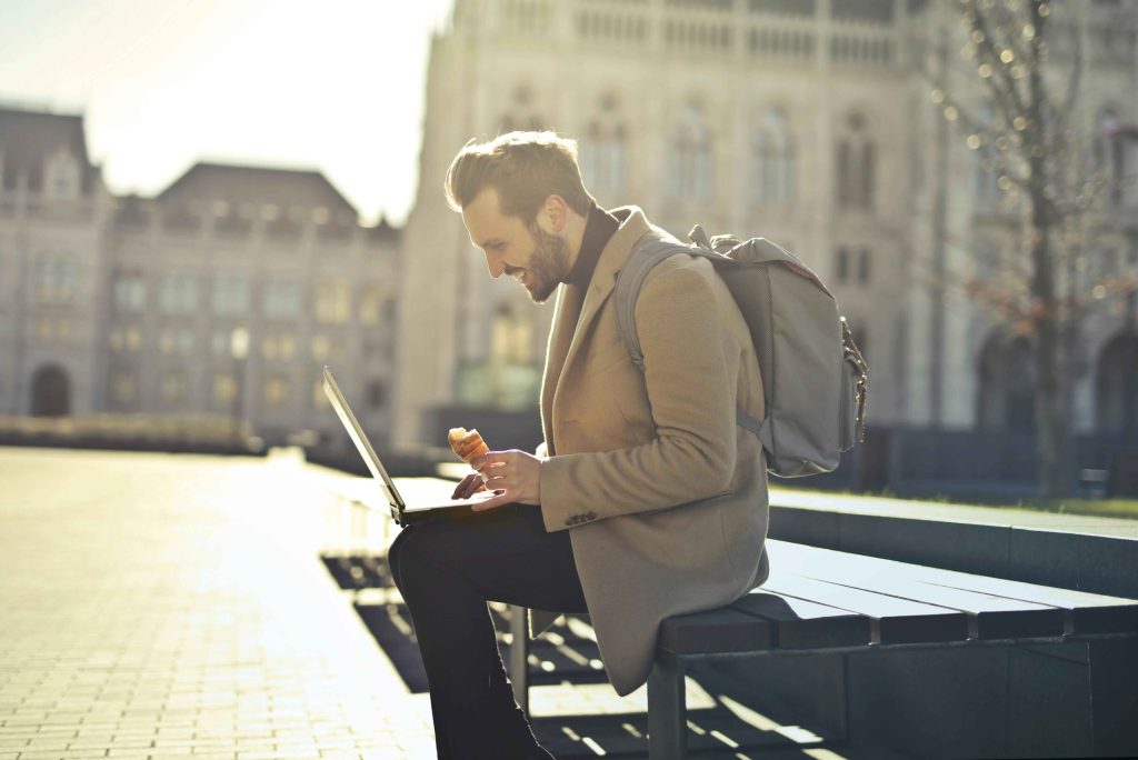 Attractive young professional man sitting on a bench and looking at his open laptop.