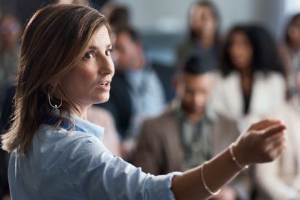 Woman speaking to a group with her hand raised as others listen