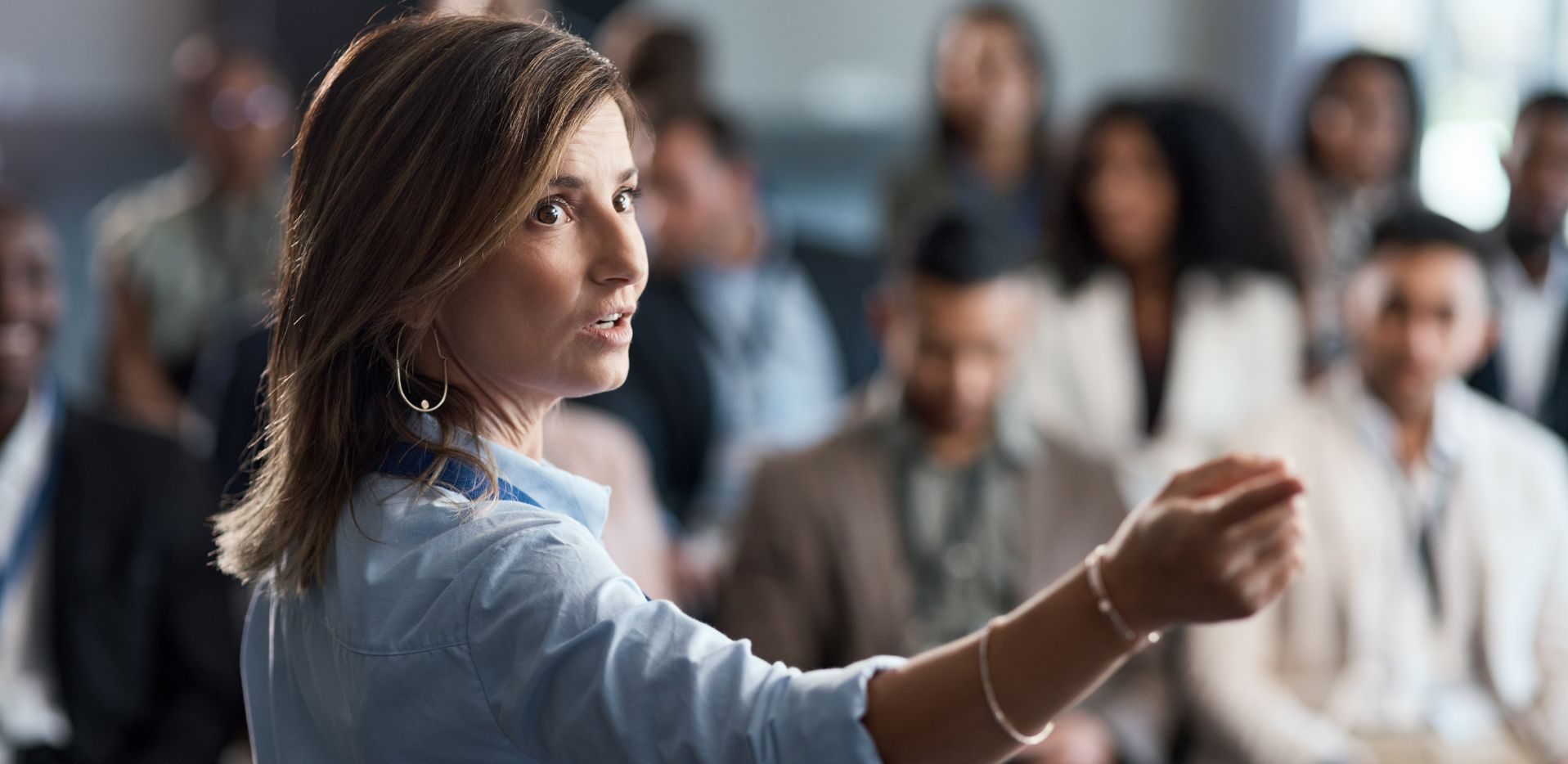 Woman speaking to a group with her hand raised as others listen