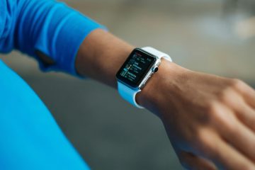 A person wearing a blue long-sleeve top checks their smartwatch with a white band, exploring time management tips for busy professionals as various app icons and information are displayed on the screen.