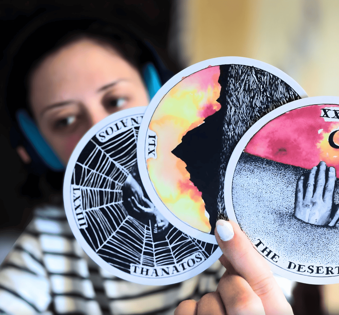 A person with light skin, dark hair, headphones, and a striped shirt holds up three illustrated tarot cards—highlighting "Messaging Magic: Your Soul-Words Tarot Reading," a session for intuitive business guidance. The focus is on the cards, not the face.