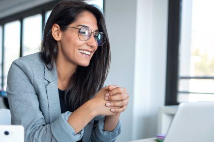 Woman smiling while speaking toward a laptop in a bright office