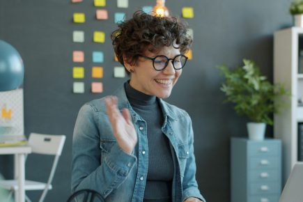 Woman smiling and waving during a video call from her desk