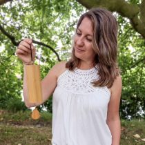 A woman stands outdoors, surrounded by greenery, holding the "Overwhelm to Calm – 1:1 Guided Meditation" product and looking at it thoughtfully.