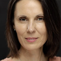 A woman with straight, shoulder-length brown hair wearing a peach lace top and delicate necklace poses in front of a dark background, smiling slightly as she promotes "Clearing Stress Naturally.