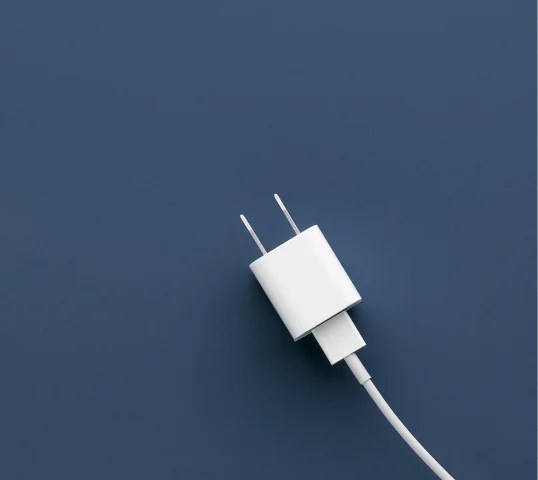 A white phone charger with a plug and attached cable lies diagonally on a plain, dark blue background, ready to keep your devices charged for plentiful online wellbeing.