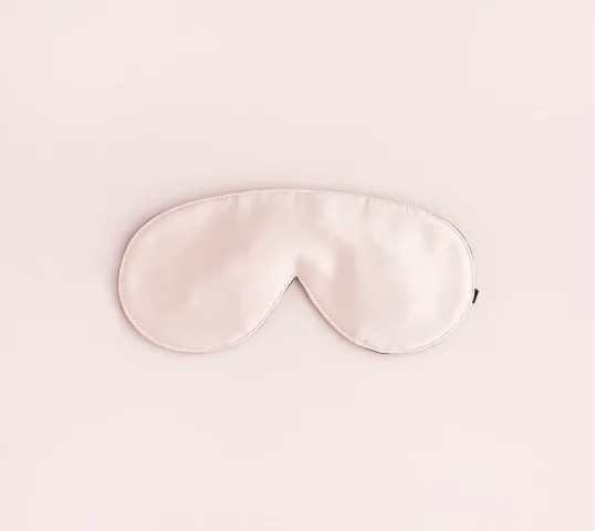 A pale pink silk sleep mask, designed for plentiful rest and enhanced wellbeing, is laid flat against a matching light pink background.