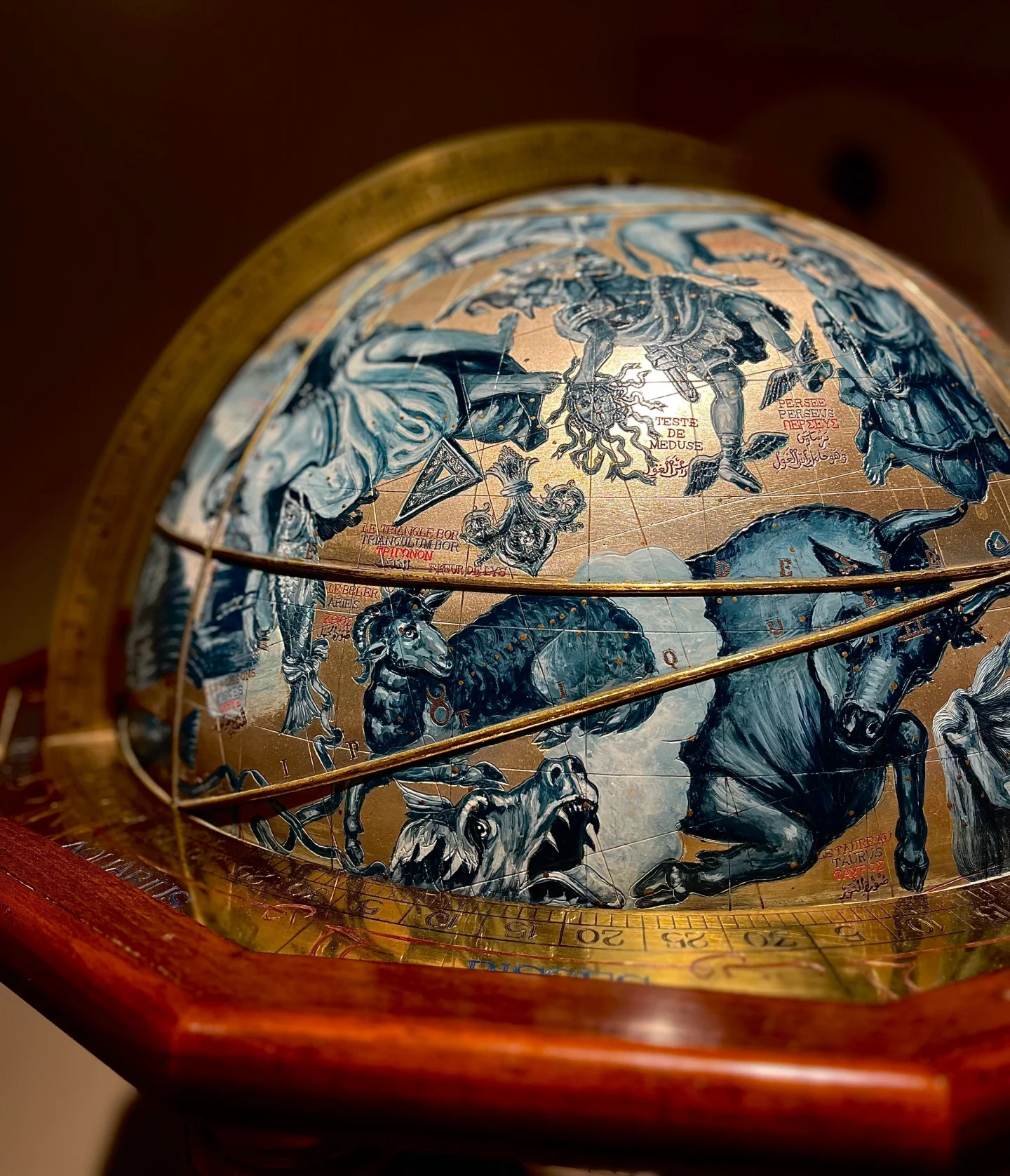 A close-up of a celestial globe featuring detailed illustrations of zodiac constellations, including a bull and various mythological figures, with gold and blue tones. The globe is mounted on a wooden stand.