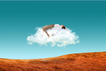 A person lies on their back atop a fluffy cloud floating above an orange, grassy landscape under a clear blue sky.
