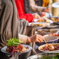 Guests help themselves to vibrant, colorful salads and assorted dishes from the buffet table at the Somerset Food & Wellness Retreat: Foraging, their hands and plates in focus as they enjoy a casual, social atmosphere.